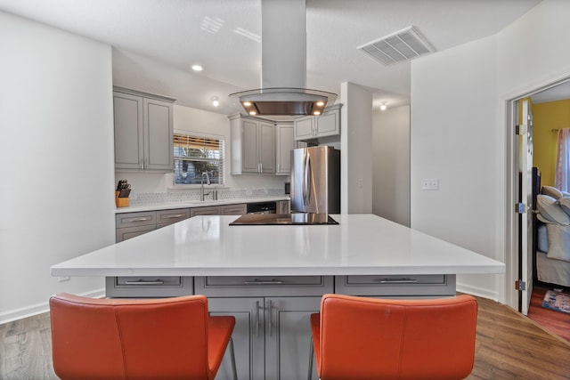 kitchen featuring island range hood, appliances with stainless steel finishes, gray cabinetry, a breakfast bar, and a kitchen island