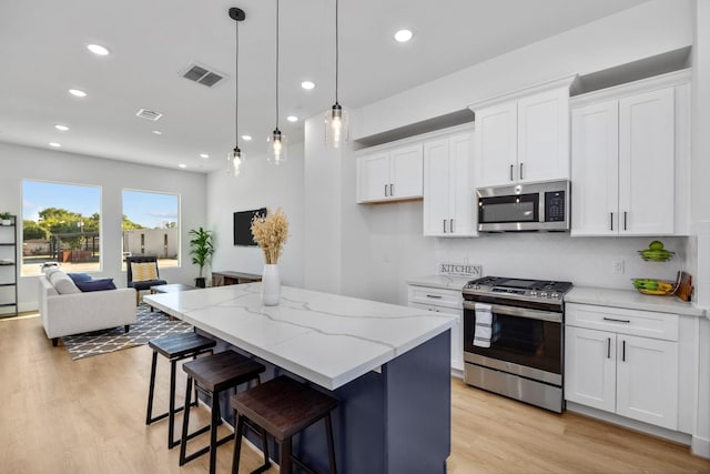 kitchen featuring light stone countertops, appliances with stainless steel finishes, white cabinets, a kitchen island, and hanging light fixtures