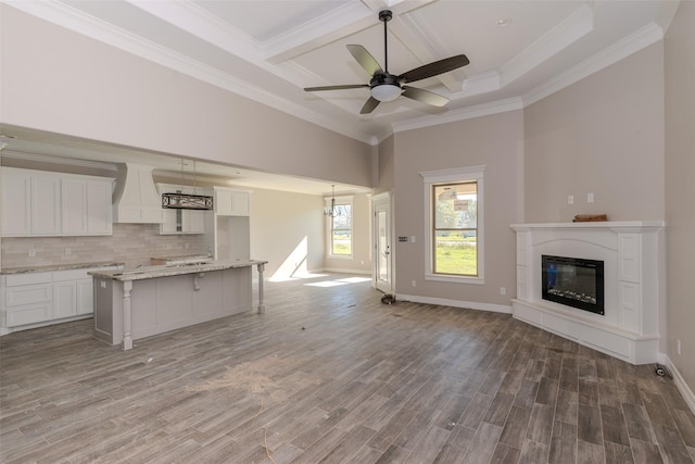 unfurnished living room featuring crown molding, ceiling fan, dark wood-type flooring, and coffered ceiling