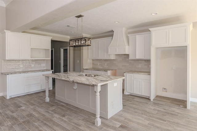 kitchen with light wood-type flooring, white cabinetry, a kitchen island with sink, and premium range hood