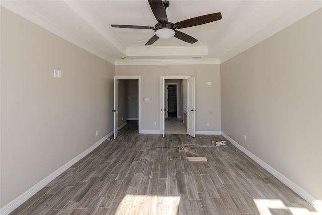 unfurnished bedroom featuring a tray ceiling, ceiling fan, crown molding, and dark wood-type flooring