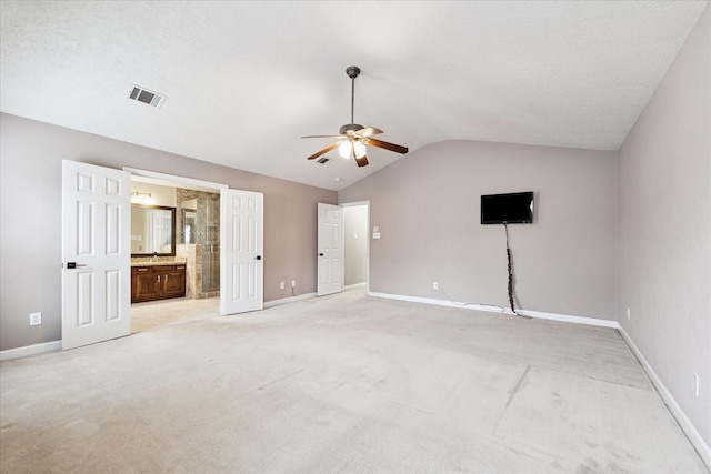 interior space featuring vaulted ceiling, connected bathroom, light colored carpet, and ceiling fan