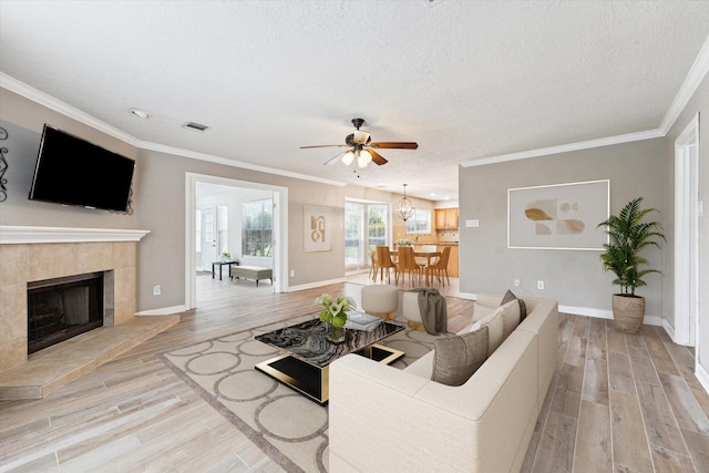 living room featuring a tile fireplace, ornamental molding, a textured ceiling, and light hardwood / wood-style flooring