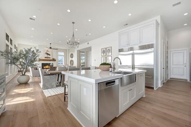 kitchen featuring white cabinetry, sink, light hardwood / wood-style floors, a center island with sink, and appliances with stainless steel finishes