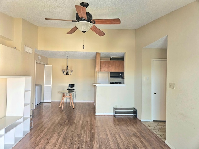 unfurnished living room with a textured ceiling, ceiling fan, a towering ceiling, and dark wood-type flooring