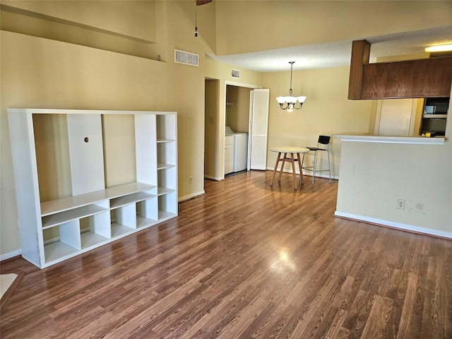 unfurnished living room featuring a towering ceiling, a textured ceiling, wood-type flooring, a notable chandelier, and independent washer and dryer