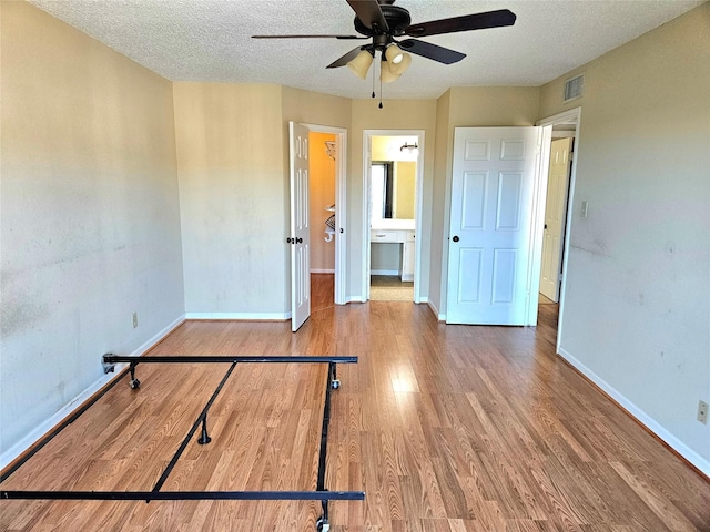 unfurnished bedroom with ceiling fan, wood-type flooring, a textured ceiling, and ensuite bath