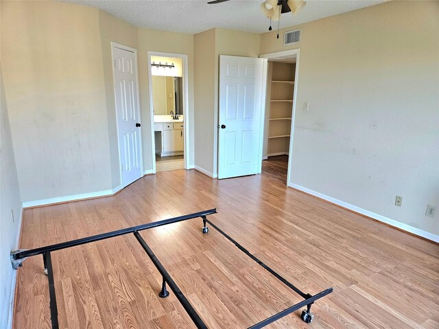 unfurnished bedroom with ensuite bathroom, ceiling fan, a textured ceiling, and hardwood / wood-style flooring