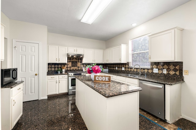 kitchen featuring stainless steel appliances, dark stone counters, a kitchen island, white cabinets, and sink