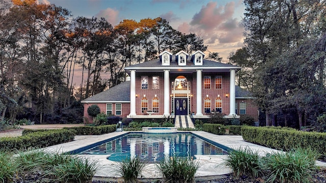 pool at dusk featuring an in ground hot tub