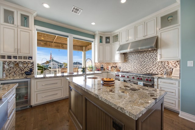 kitchen with beverage cooler, under cabinet range hood, double oven range, dark wood finished floors, and a sink