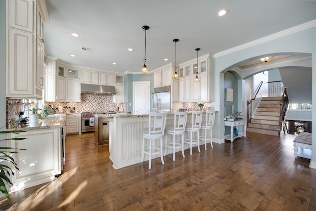 kitchen with premium appliances, visible vents, arched walkways, backsplash, and under cabinet range hood