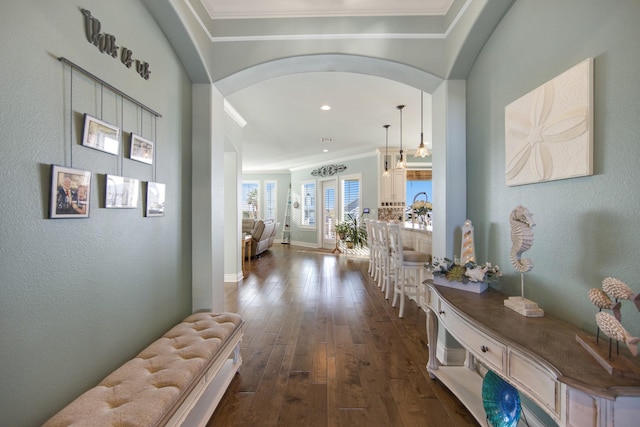 corridor with arched walkways, ornamental molding, dark wood-style floors, and baseboards