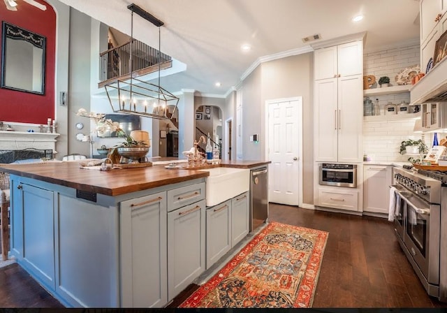 kitchen featuring white cabinets, wood counters, an island with sink, and appliances with stainless steel finishes