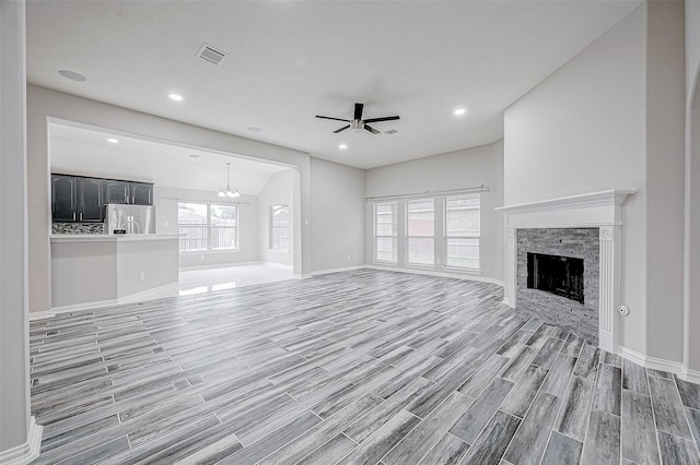 unfurnished living room featuring ceiling fan with notable chandelier, lofted ceiling, and a fireplace