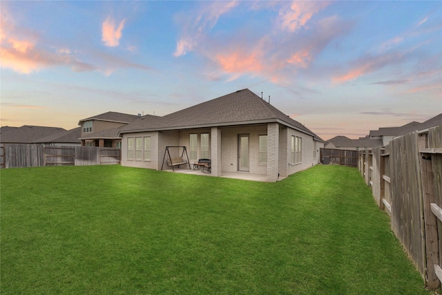 back house at dusk featuring a patio area and a lawn