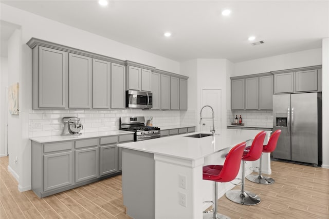 kitchen with gray cabinetry, a kitchen breakfast bar, sink, an island with sink, and appliances with stainless steel finishes