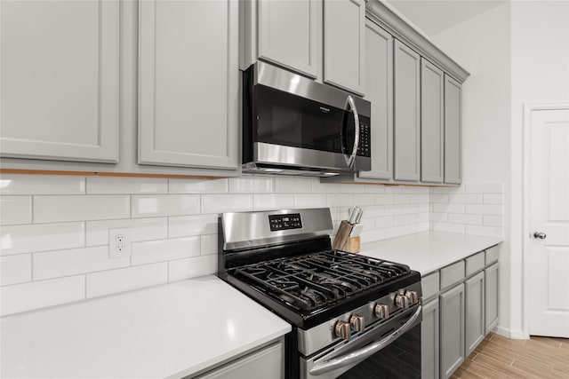 kitchen featuring gray cabinets, light wood-type flooring, appliances with stainless steel finishes, and tasteful backsplash