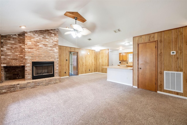 unfurnished living room featuring carpet, vaulted ceiling, ceiling fan, wooden walls, and a fireplace