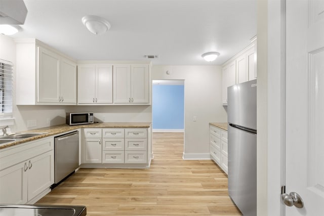 kitchen with stainless steel appliances, white cabinetry, and light wood-type flooring