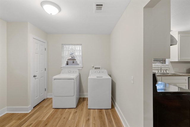 clothes washing area with sink, washing machine and dryer, and light hardwood / wood-style floors