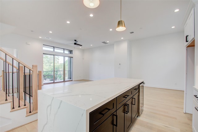 kitchen with light stone counters, pendant lighting, ceiling fan, light hardwood / wood-style floors, and white cabinets