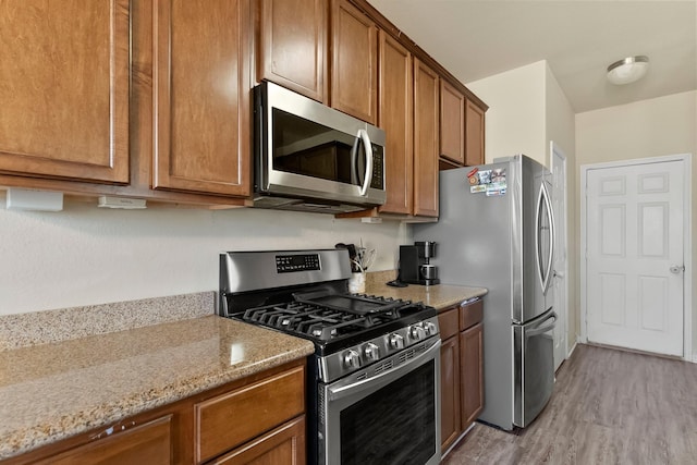 kitchen with light hardwood / wood-style floors, light stone counters, and stainless steel appliances