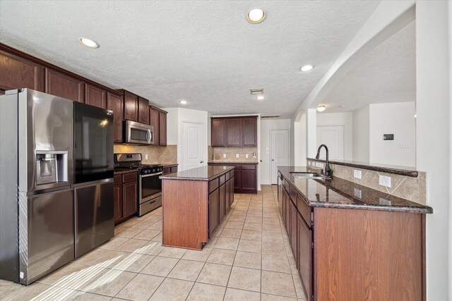 kitchen with a kitchen island with sink, sink, light tile patterned floors, and appliances with stainless steel finishes