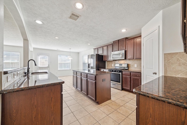 kitchen featuring sink, hanging light fixtures, backsplash, a center island with sink, and appliances with stainless steel finishes