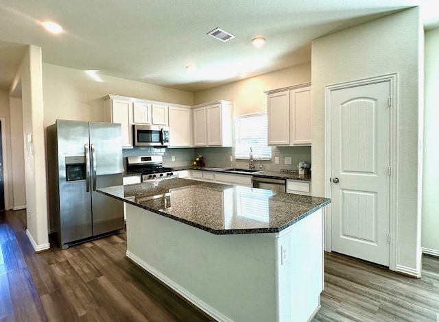 kitchen with white cabinets, appliances with stainless steel finishes, dark wood-type flooring, a center island, and a sink