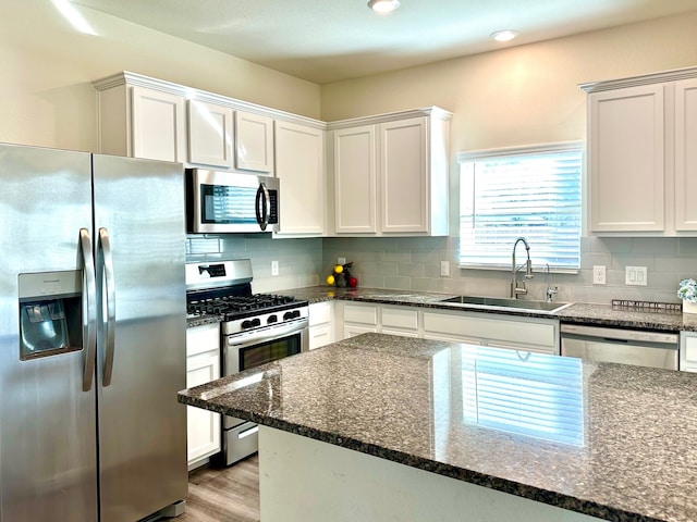 kitchen with appliances with stainless steel finishes, white cabinets, a sink, and backsplash