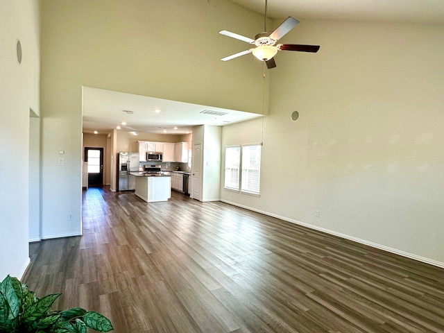 unfurnished living room with dark wood-type flooring, a high ceiling, visible vents, a ceiling fan, and baseboards