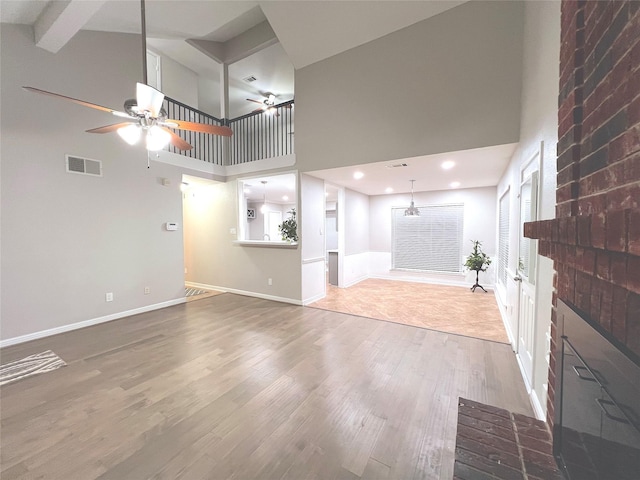 unfurnished living room featuring beamed ceiling, ceiling fan, wood-type flooring, and a high ceiling