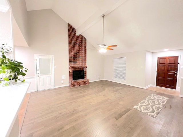 unfurnished living room featuring a brick fireplace, ceiling fan, beam ceiling, high vaulted ceiling, and light hardwood / wood-style flooring