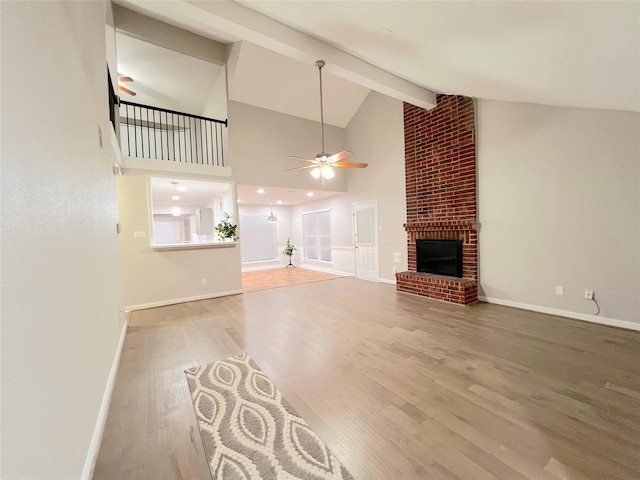 unfurnished living room featuring a brick fireplace, ceiling fan, beam ceiling, wood-type flooring, and high vaulted ceiling