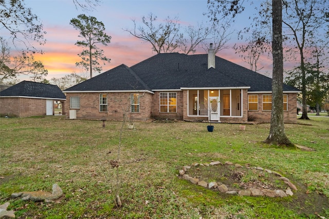 back house at dusk with a sunroom and a lawn