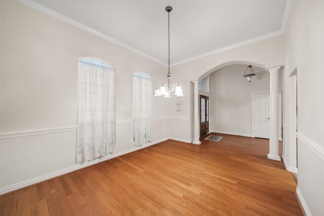 unfurnished dining area featuring ornate columns, crown molding, a chandelier, and hardwood / wood-style flooring