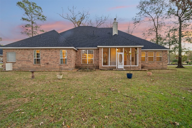 back house at dusk with a sunroom and a yard