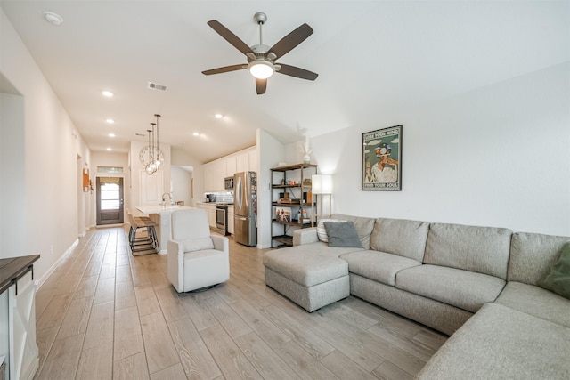 living room with ceiling fan, light hardwood / wood-style floors, and vaulted ceiling