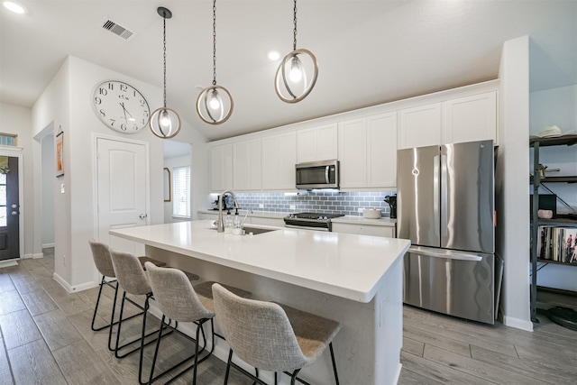 kitchen with white cabinetry, stainless steel appliances, pendant lighting, a kitchen island with sink, and light wood-type flooring