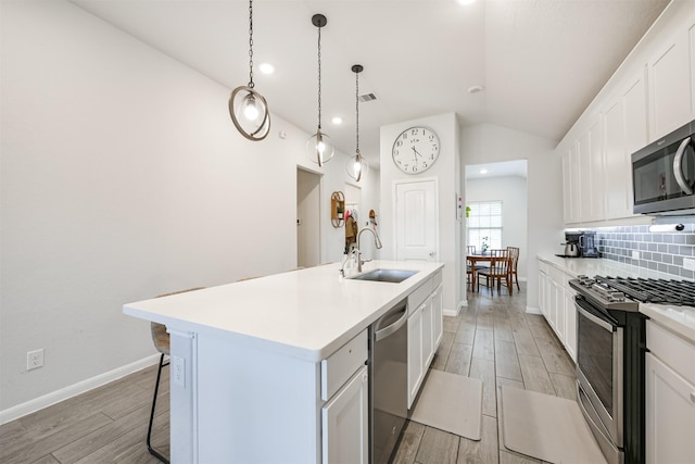 kitchen with sink, hanging light fixtures, an island with sink, white cabinetry, and stainless steel appliances