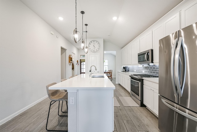 kitchen with a kitchen island with sink, a kitchen breakfast bar, sink, vaulted ceiling, and appliances with stainless steel finishes