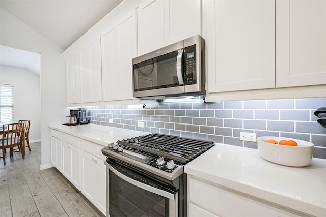 kitchen featuring appliances with stainless steel finishes, white cabinetry, vaulted ceiling, and light hardwood / wood-style flooring