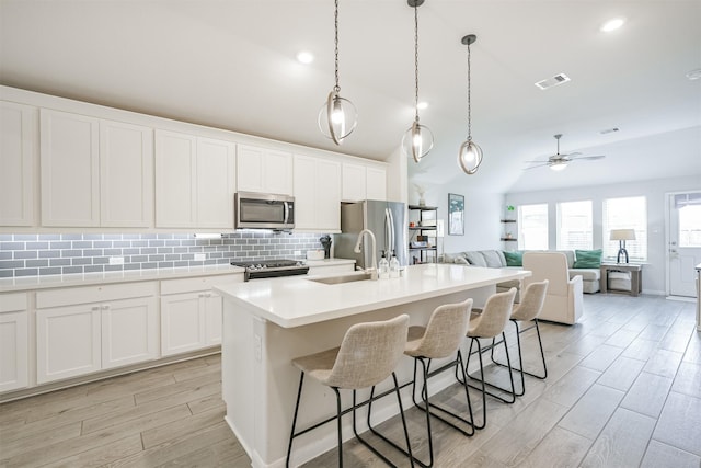 kitchen with stainless steel appliances, ceiling fan, sink, a center island with sink, and white cabinetry