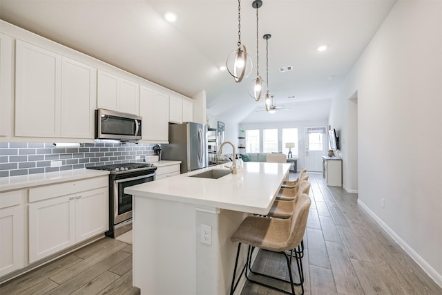 kitchen with appliances with stainless steel finishes, ceiling fan, sink, white cabinetry, and an island with sink