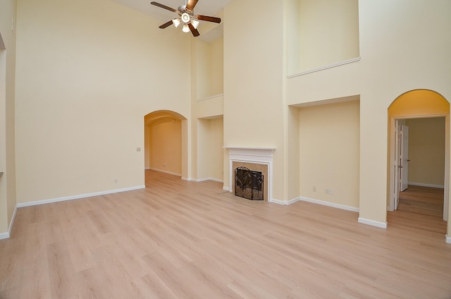 unfurnished living room with ceiling fan, a high ceiling, and light hardwood / wood-style flooring