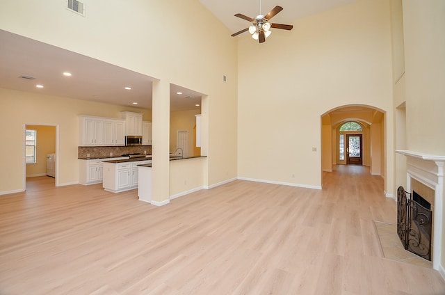 unfurnished living room featuring a high ceiling, light hardwood / wood-style flooring, ceiling fan, and a tiled fireplace