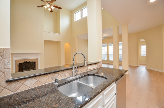 kitchen featuring dishwasher, dark stone counters, sink, a fireplace, and white cabinetry