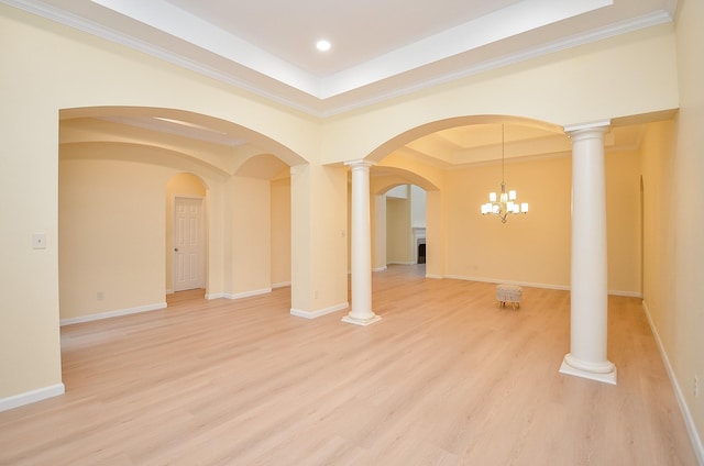 empty room with a notable chandelier, ornate columns, wood-type flooring, and a tray ceiling