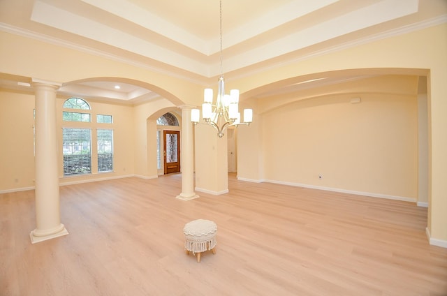 interior space with decorative columns, a chandelier, a tray ceiling, hardwood / wood-style flooring, and ornamental molding